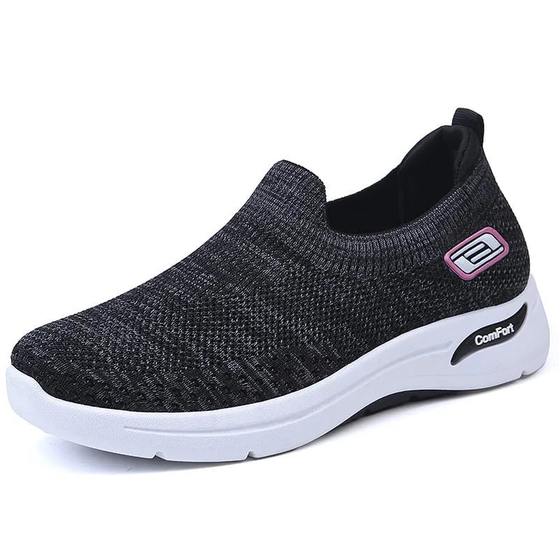 Side view of a black knit slip-on trainer with purple accent badge and white midsole