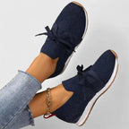 Side view of navy knit slip-on trainer with bow lace detail, white midsole and tan outsole, worn on foot