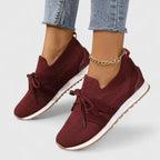 Close-up of burgundy knit sneakers with bow tie laces, white sole and tan rubber outsole on model's feet
