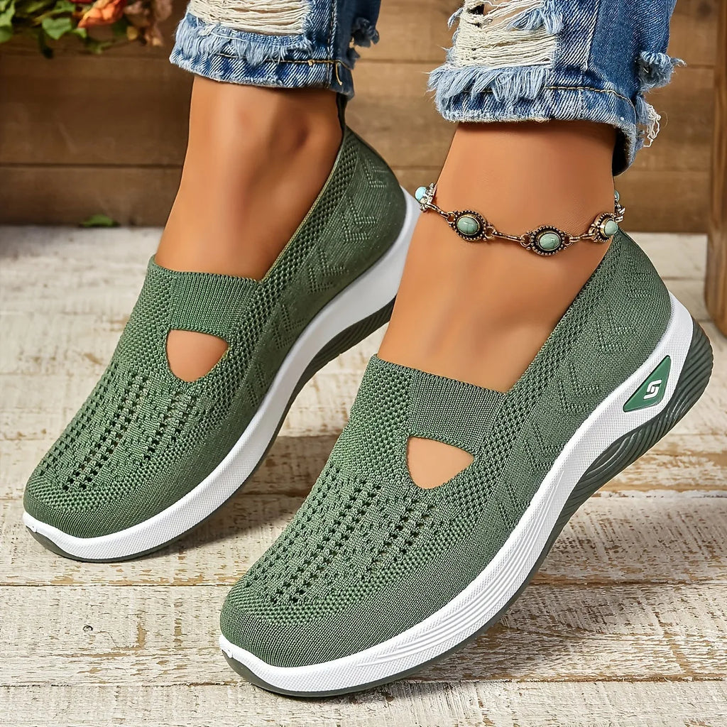 Olive green knit slip-on trainers with side cut-out and white ridged sole, shown from the front on model's feet
