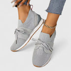 Pair of light grey knit trainers with bow lacing and cushioned white sole, shown from above on bare feet