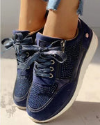 Close-up of navy blue trainer with sparkly ribbon-style laces, side zip and diamante detailing on the toe