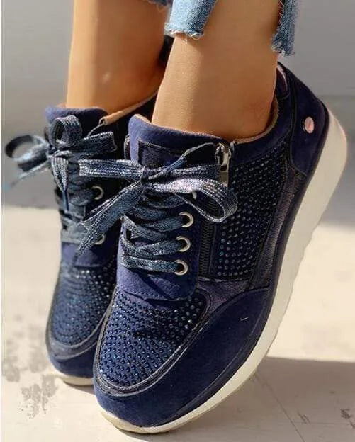 Close-up of navy blue trainer with sparkly ribbon-style laces, side zip and diamante detailing on the toe