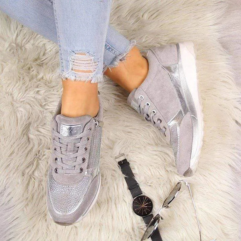 Grey and silver trainer with metallic heel tab and side zip, textured sole on wooden floor