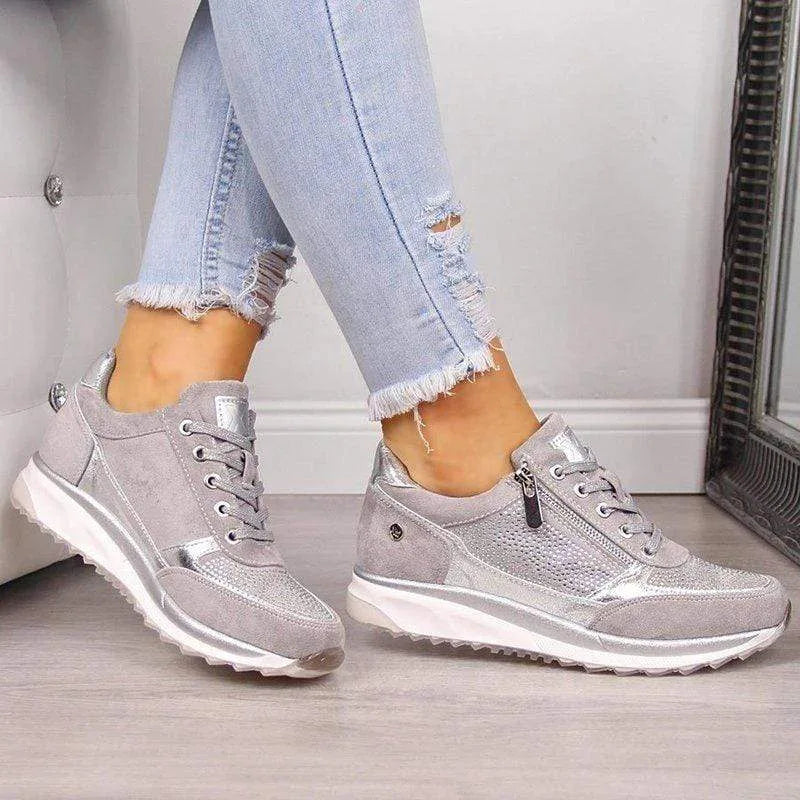 Silver metallic trainer with suede panels, lace-up front and chunky sole held in hand on faux fur rug