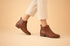 Side view of tan brown leather ankle boots with side zip and stacked heel, worn with cream trousers