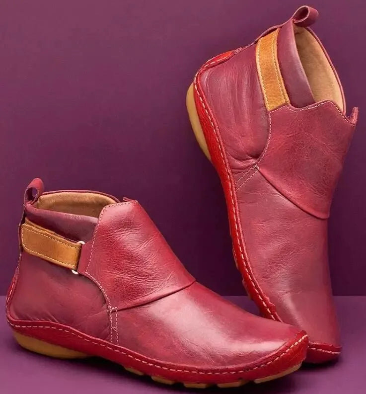 Pair of brown leather ankle boots with tan strap standing on a purple surface