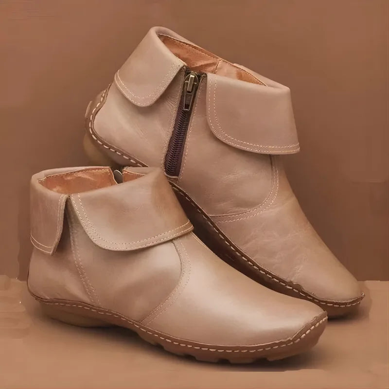 Beige leather ankle boots with foldover collar, contrast stitching and side zip fastening on a light backdrop