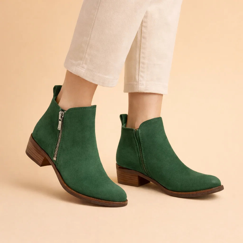 Dark green suede ankle boots with silver side zip and stacked heel, paired with cream trousers