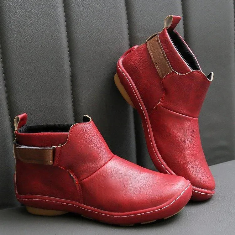 Blue-grey leather ankle boots with brown side strap on an orange background