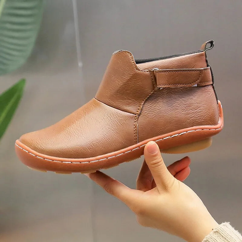 Close-up of a hand holding a brown leather ankle boot to show texture and sole