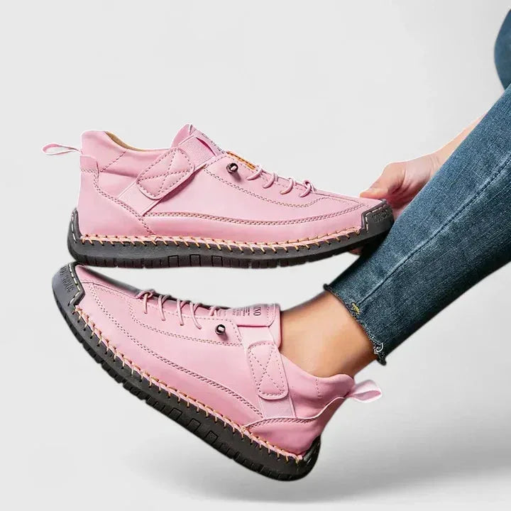 Side view of pink leather lace-up trainers with hand-stitched detailing and a grey ridged sole, shown on a model's foot