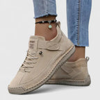 Beige suede lace-up trainers with tonal stitching and a textured rubber sole, worn with denim