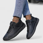 Black leather lace-up trainers with hand-stitched panels and matching sole, shown from above on the foot