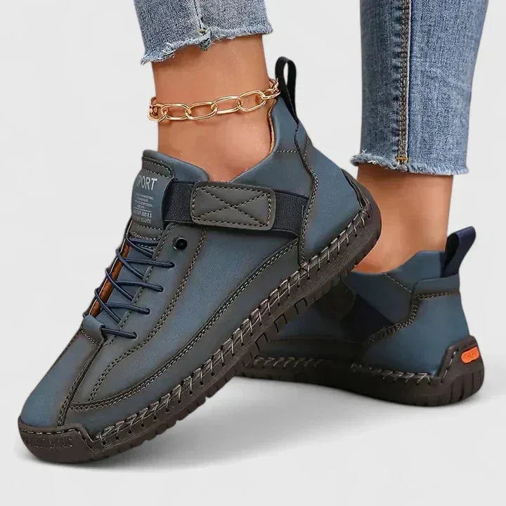 Slate blue leather lace-up trainers with orange sole detail and hook-and-loop strap, worn on the ankle