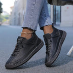 Black leather trainer with visible hand-stitch seams and lace-up front, styled with cropped denim