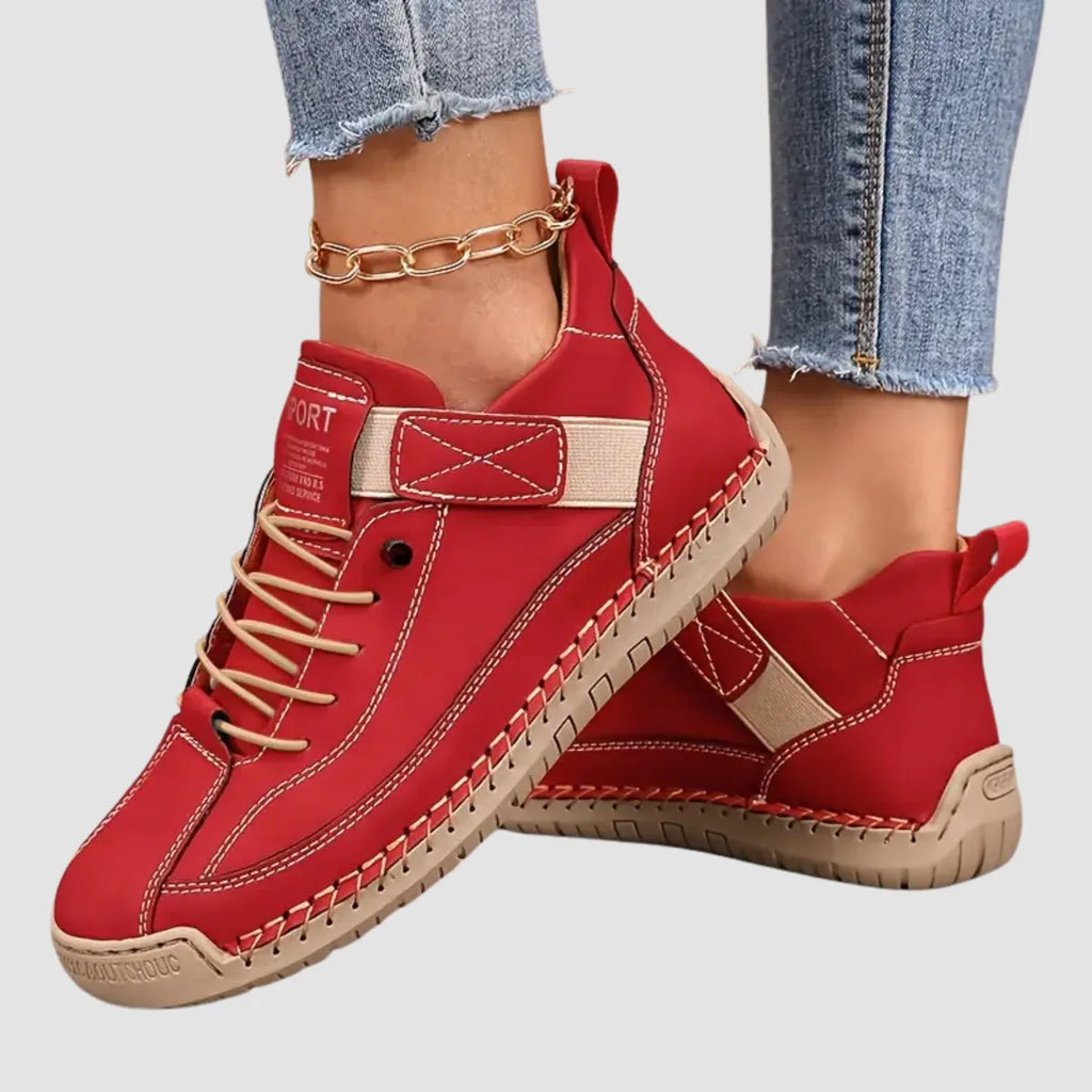 Red leather trainer paired with tan laces and elastic strap, shown against a plain grey studio background