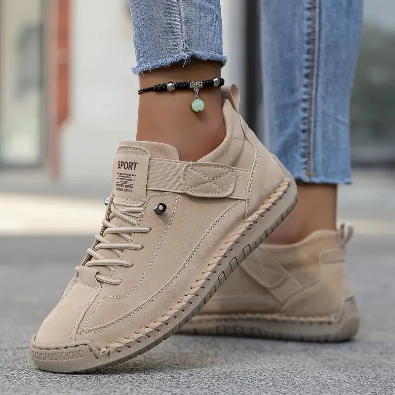 Beige suede trainer with tonal stitching, worn barefoot with rolled denim and a beaded anklet