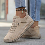 Beige suede trainer with tonal stitching, worn barefoot with rolled denim and a beaded anklet