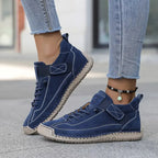 Navy blue suede trainer with tan sole and elastic strap, shown from a low side angle on pavement