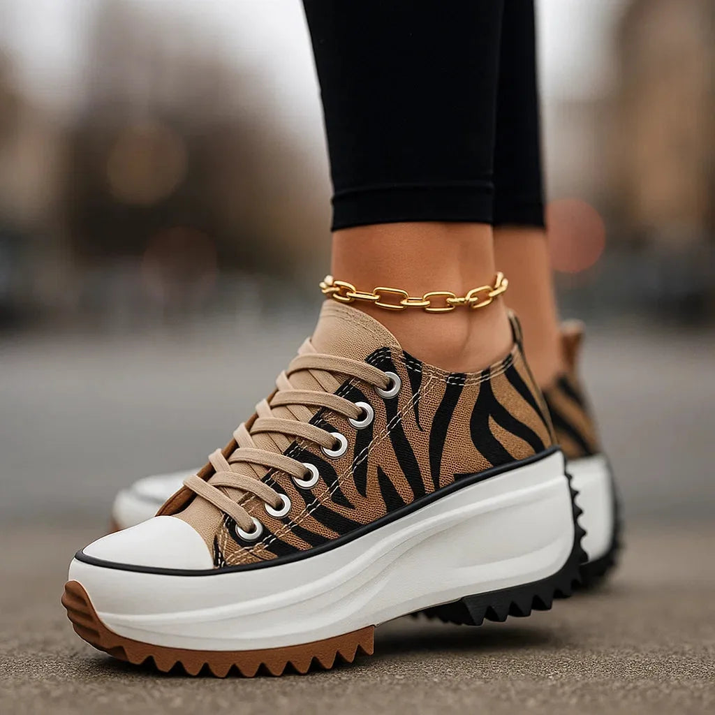 Close-up side view of tiger-print platform trainer with tan laces and chunky white ridged sole, worn with black leggings
