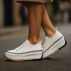 White canvas platform trainer with black trim and gum sole, shown mid-stride beneath a knitted skirt