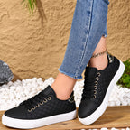 Side view of black quilted-panel trainer with white sole and gold-tone eyelets, styled with cropped jeans and a chain anklet.