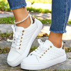 Pair of white quilted trainers with metallic gold heel tab and white laces, worn with jeans and a pearl anklet.