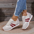 Side view of grey trainers featuring burgundy side stripes and a pale pink heel tab, styled with frayed denim.