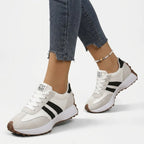 Side view of white retro trainers with black stripes and 'Stay Ready' tab, worn on foot with cropped jeans and anklet