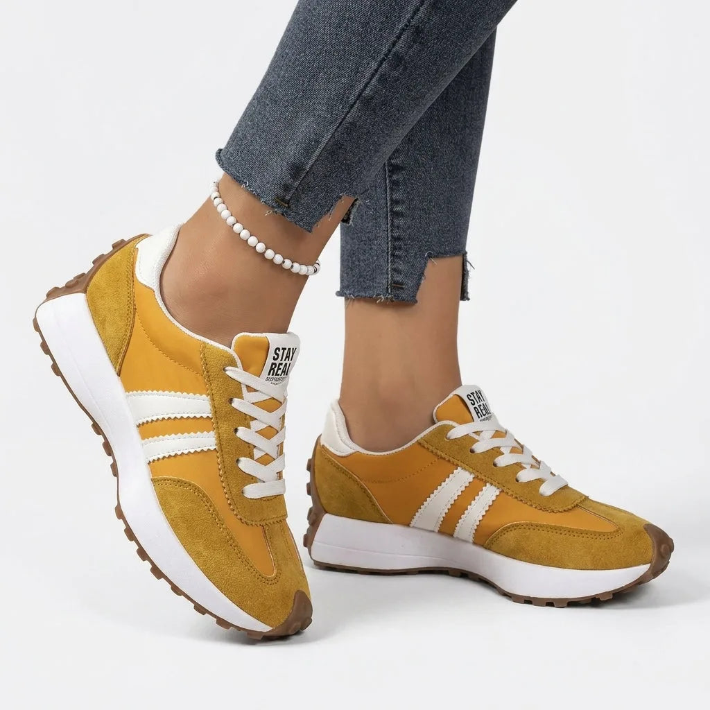 Mustard yellow suede and nylon trainers with cream stripes, worn on foot styled with cropped denim jeans
