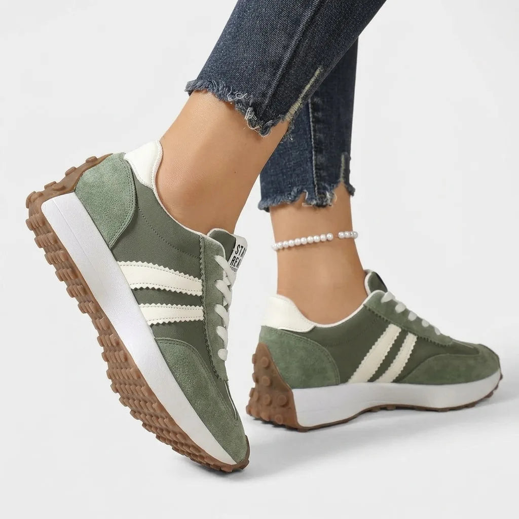 Sage green suede trainers with cream side stripes, shown from behind and side while worn with jeans
