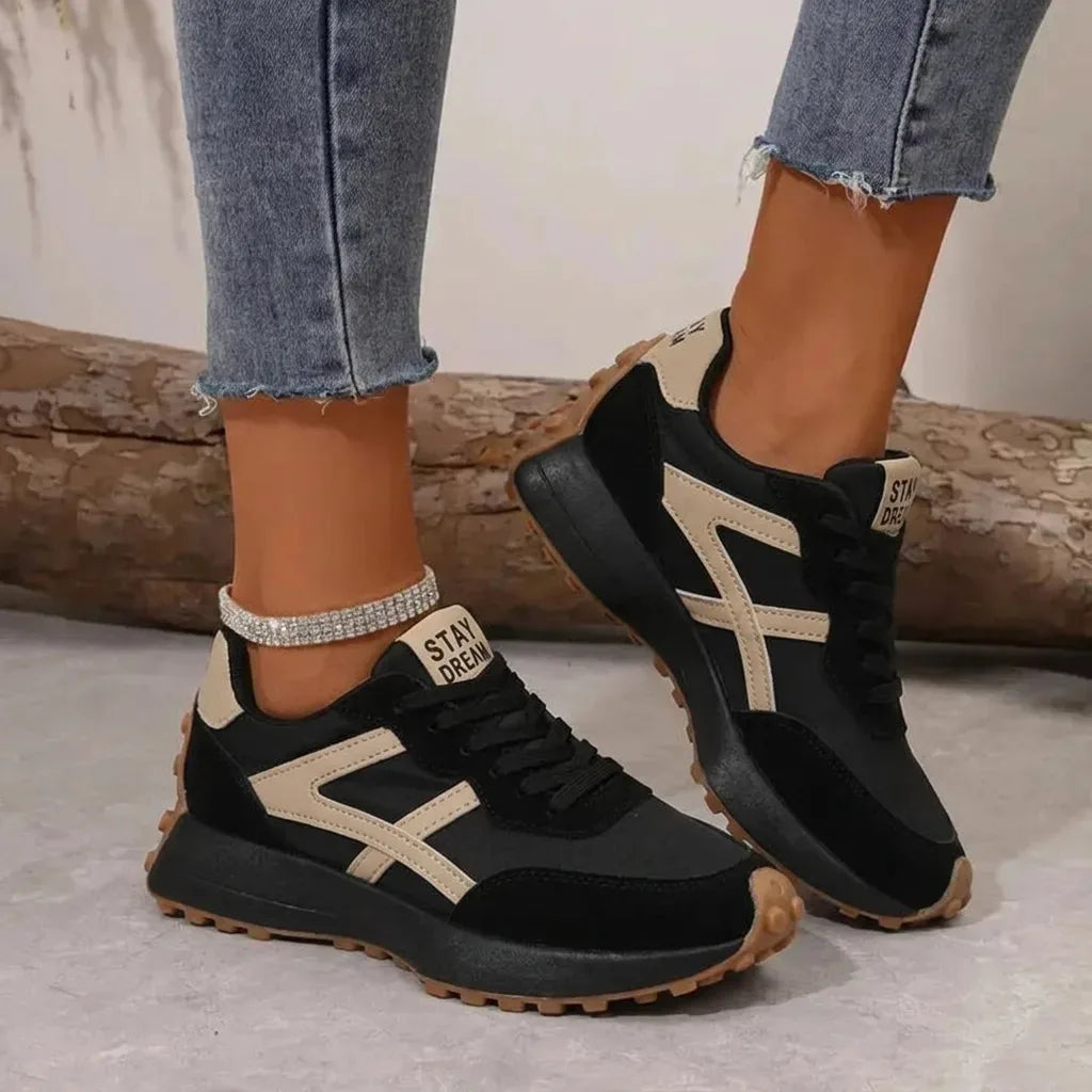 Side view of black and beige lace-up trainers with chunky gum sole, worn with cropped jeans and a diamante anklet