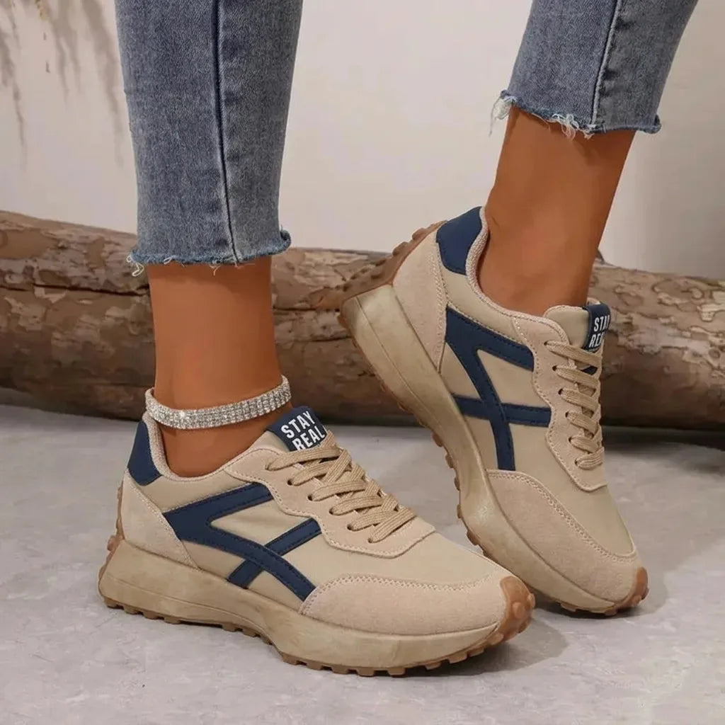 Side-by-side view of beige and navy colour-block trainers with lace-up front and ridged gum sole, worn with jeans