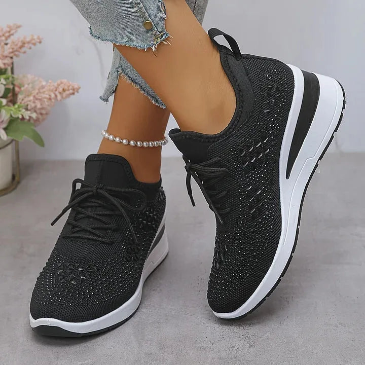 Top-down view of white rhinestone trainers being held by hand, showing knit texture and laces