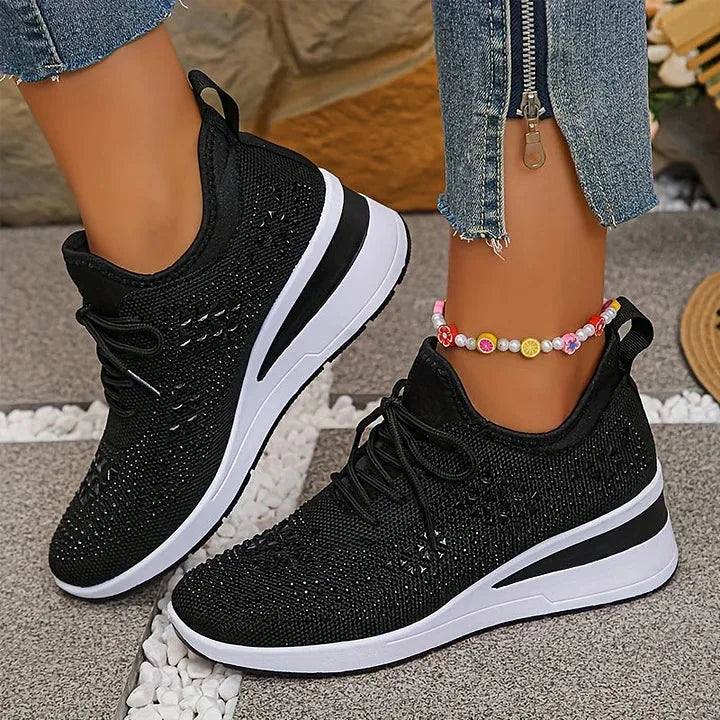 Black rhinestone trainers held in hand from above, showing sparkling star pattern and pull tab