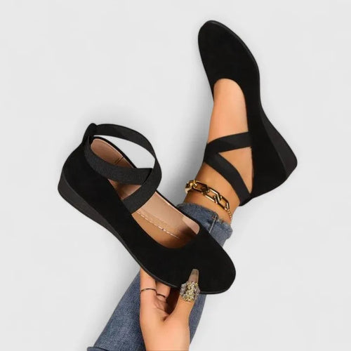 Black suede ballet flats with crossover elastic ankle straps, shown from above on model's raised feet