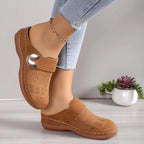 Side view of tan suede orthopedic clog showing cushioned wedge sole, gold buckle trim and contrast stitching worn with cropped jeans