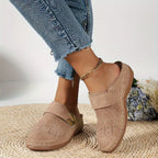 Beige suede backless clog shown on foot with gold ankle chain, styled with ripped jeans and dried flowers in the background