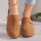 Pair of tan suede clogs with perforated detailing and gold trim displayed front-on against a wood floor backdrop