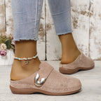Beige suede clog with gold buckle worn with beaded anklet, paired with cropped jeans against a rustic wooden wall