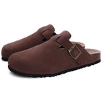 Pair of brown suede clog slippers angled to show buckle strap and ridged black outsole