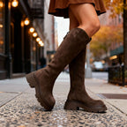 Close-up back and side angle of brown suede knee-high boots showing the zip pull and ridged outsole texture