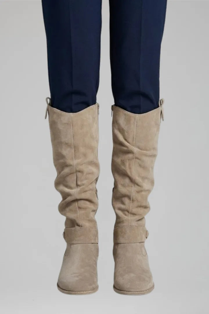Front view of beige suede knee-high boots with ruched shaft worn under tailored navy trousers
