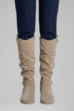 Front view of beige suede knee-high boots with ruched shaft worn under tailored navy trousers