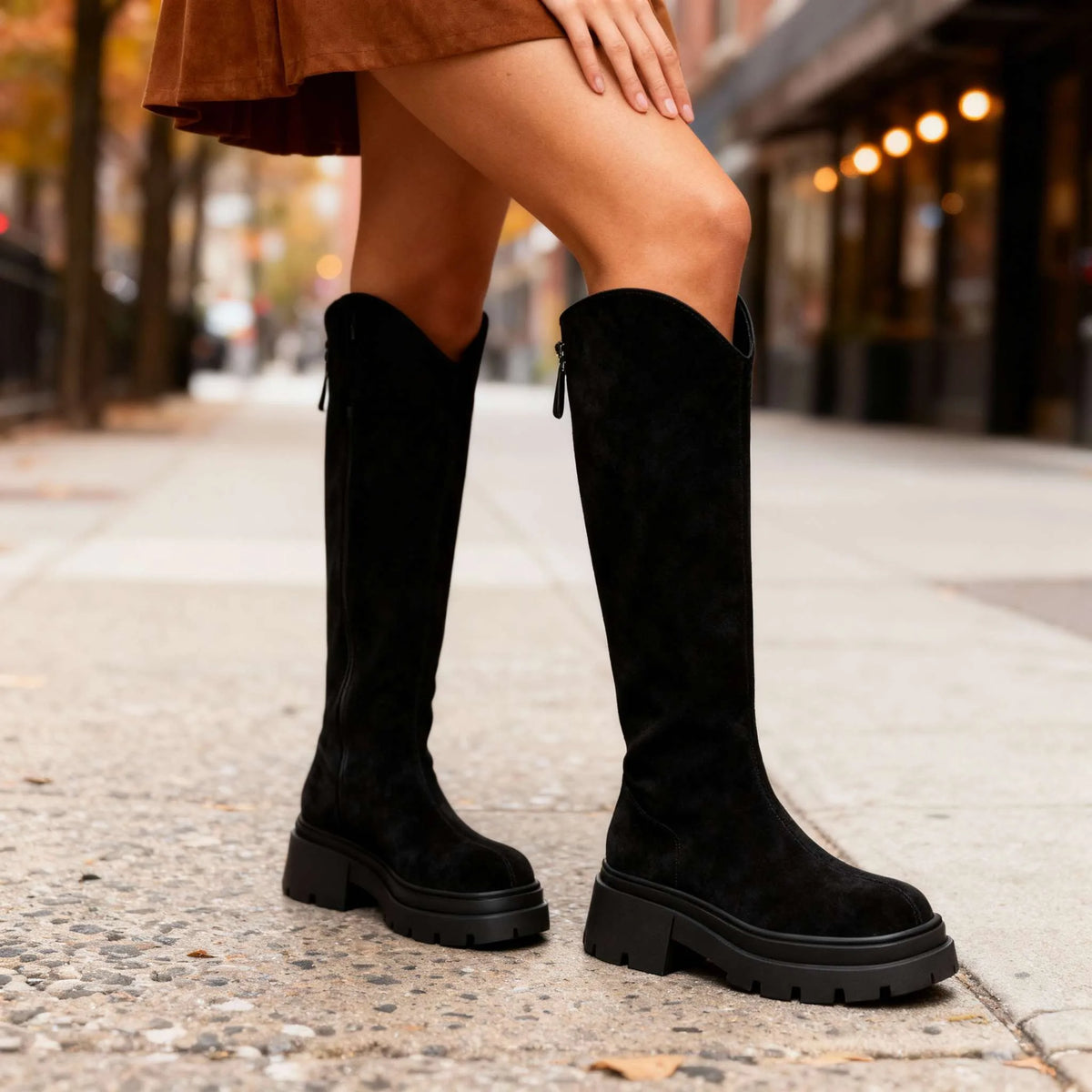 Black suede knee-high boots photographed from the side, highlighting the tall shaft and ridged tread sole
