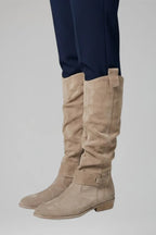 Side profile of beige suede knee-high boot showing slouch shaft, low block heel and rounded toe
