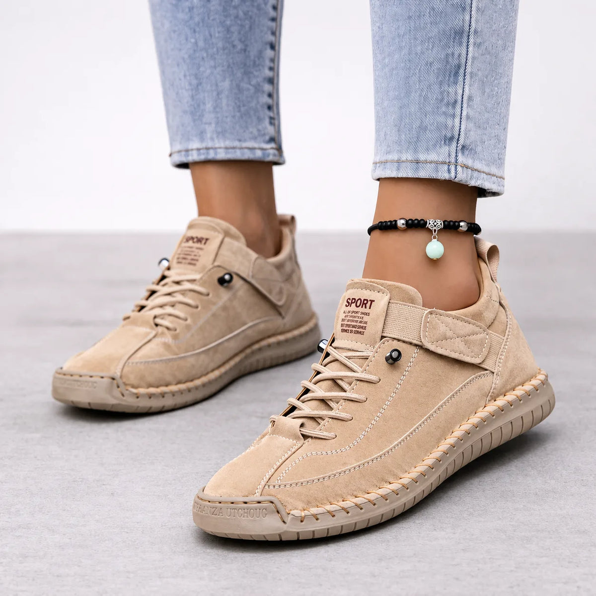 Close-up side view of beige suede lace-up trainers with contrast stitching and a chunky rubber sole, worn with cropped jeans