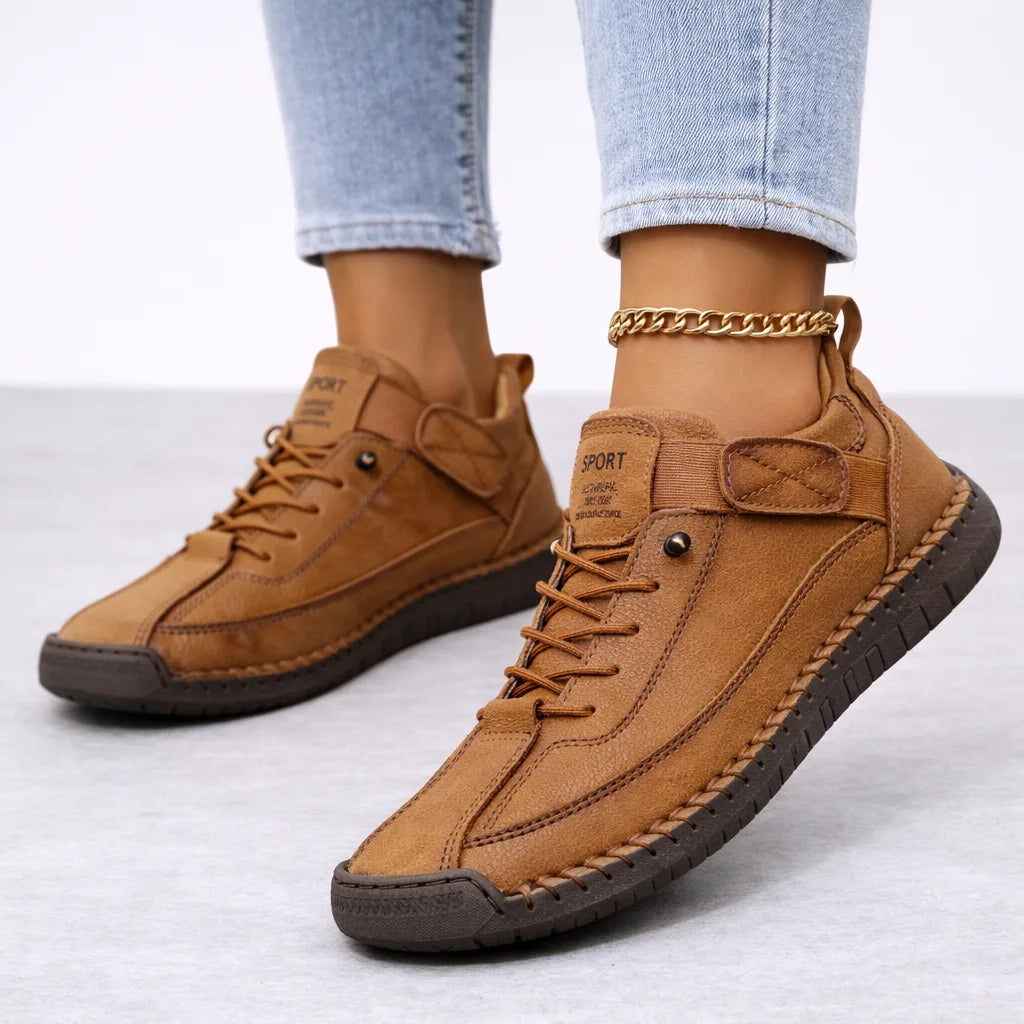 Tan brown suede trainers shown on feet with a woven whipstitch trim and dark ridged outsole, paired with light denim