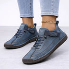 Navy blue suede lace-up trainers with a hook-and-loop ankle strap and brown textured sole, styled with turned-up jeans